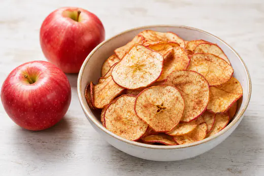 Crisp cinnamon apple chips in a bowl with whole red apples nearby