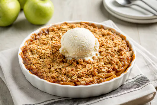 Baked apple crisp with a golden oat topping in a small round dish with vanilla ice cream