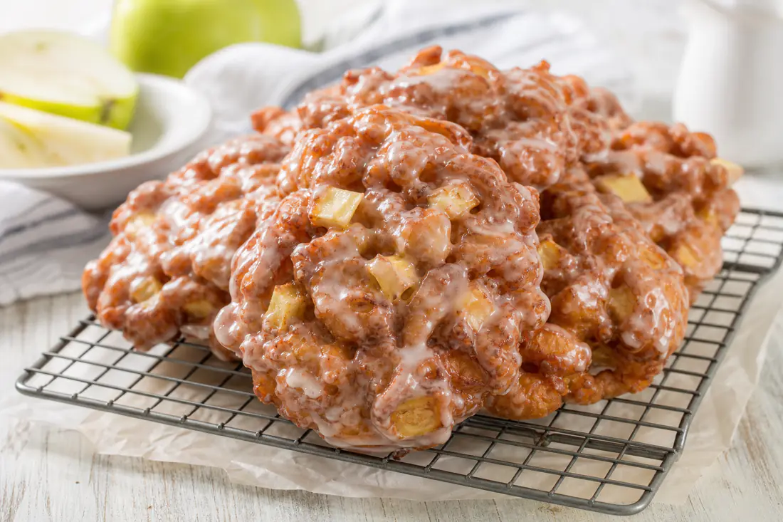 Glazed apple fritters with visible apple pieces on a wire rack