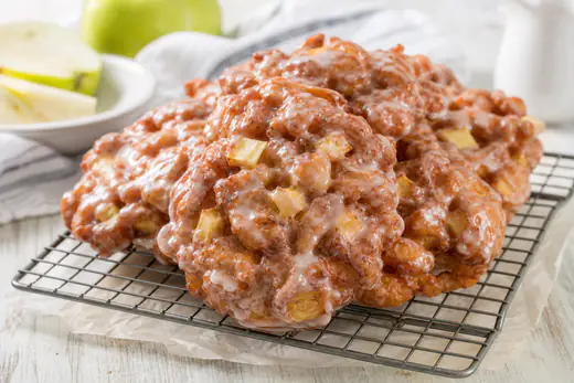 Glazed apple fritters with visible apple pieces on a wire rack
