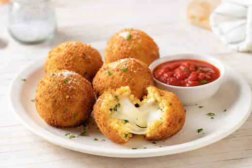 Round breaded arancini, one cut open to show melted mozzarella, with marinara sauce