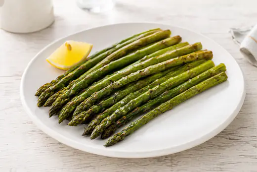Roasted asparagus spears with lightly browned tips and a lemon wedge on a white plate
