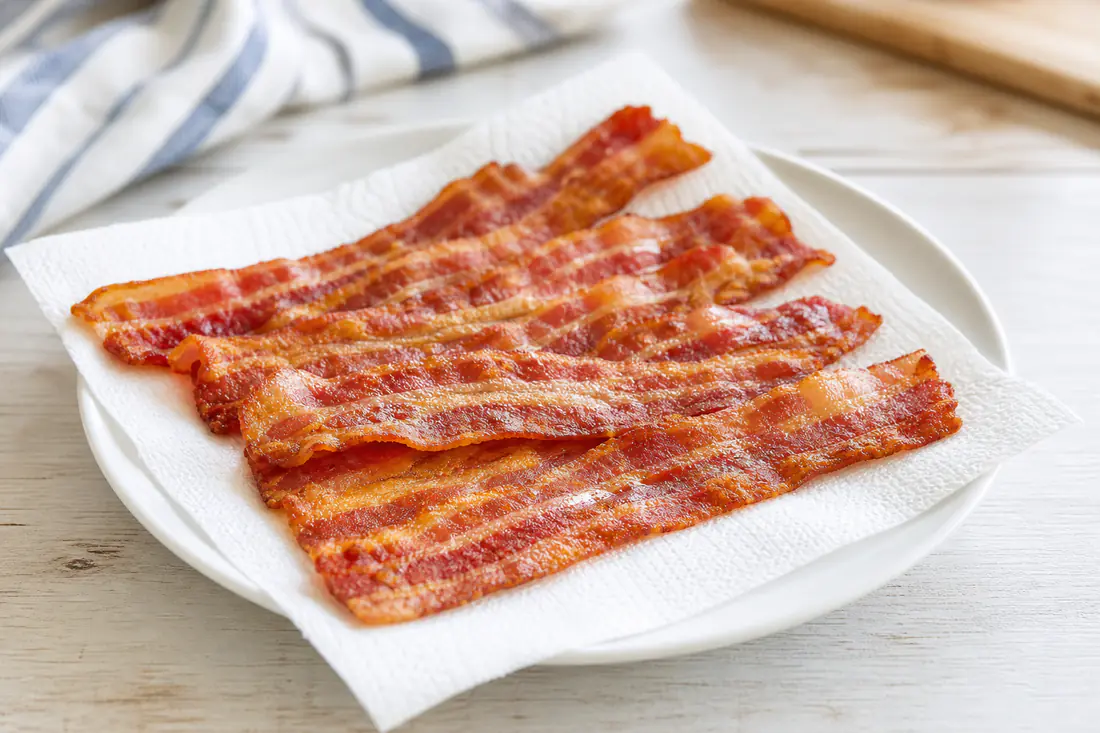 Crispy cooked bacon strips on a white plate lined with a paper towel