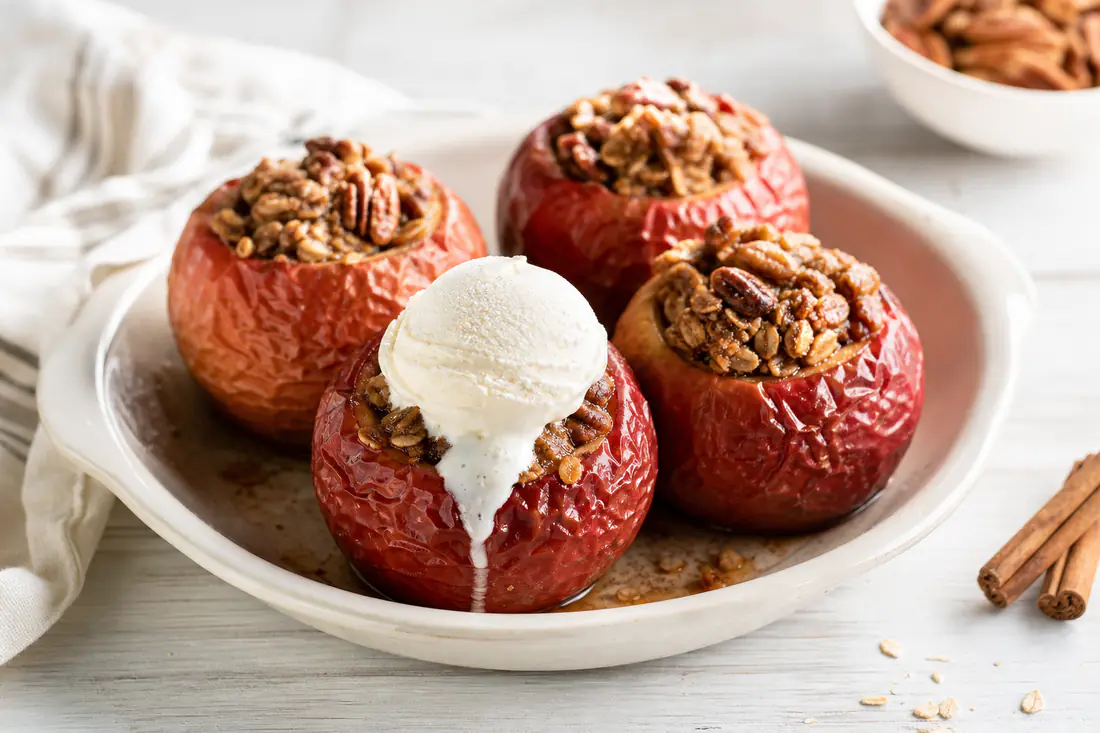 Four whole baked apples stuffed with oats, pecans and cinnamon, one with a scoop of vanilla ice cream