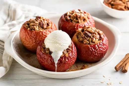 Four whole baked apples stuffed with oats, pecans and cinnamon, one with a scoop of vanilla ice cream