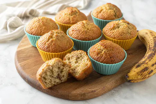 Domed banana muffins with golden brown tops in silicone cups, with a ripe banana beside them