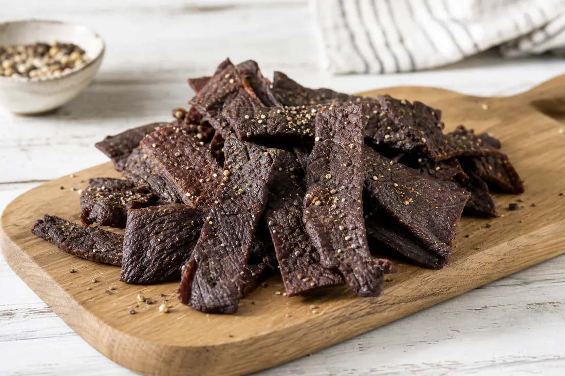Dark, chewy strips of homemade beef jerky piled on a wooden board