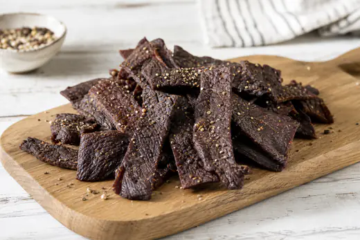 Dark, chewy strips of homemade beef jerky piled on a wooden board