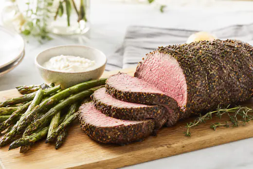 Sliced herb-crusted beef tenderloin roast with a rosy pink center on a serving board