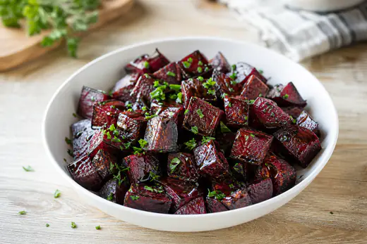 Roasted beet cubes drizzled with balsamic vinegar in a white bowl