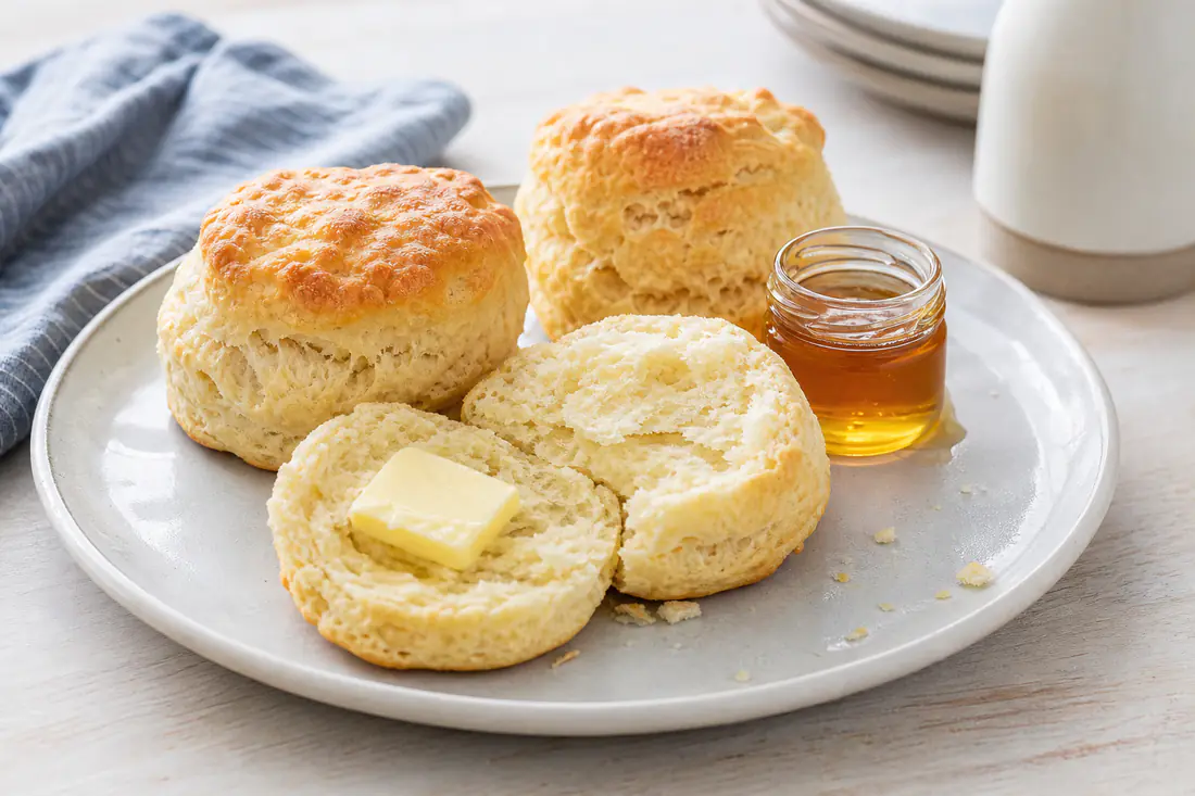 Tall golden buttermilk biscuits, one split open to show flaky layers, with butter and honey