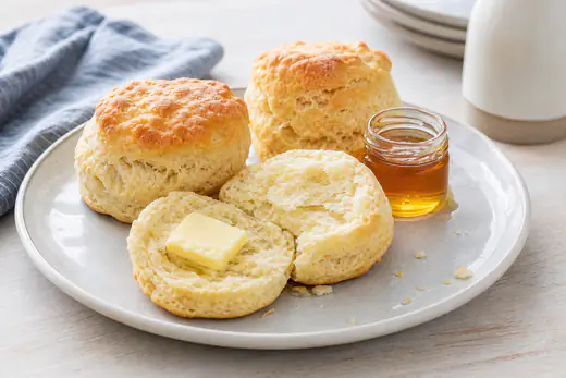 Tall golden buttermilk biscuits, one split open to show flaky layers, with butter and honey