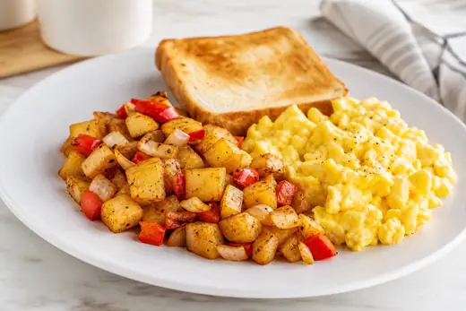 Crispy diced breakfast potatoes with onions and red peppers on a plate with eggs