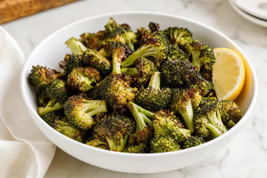 Roasted broccoli florets with browned crispy tips and a lemon wedge on a white plate