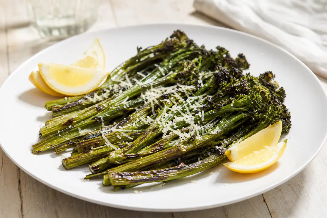 Charred broccolini stalks with lemon wedges and grated Parmesan on a white plate