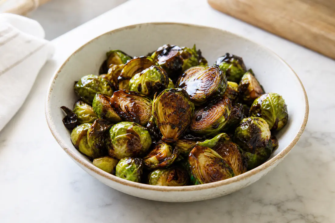 Halved roasted brussels sprouts with dark crispy leaves and a balsamic glaze in a bowl