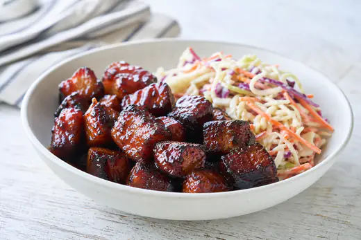 Glossy cubes of pork belly burnt ends coated in dark barbecue sauce in a white bowl