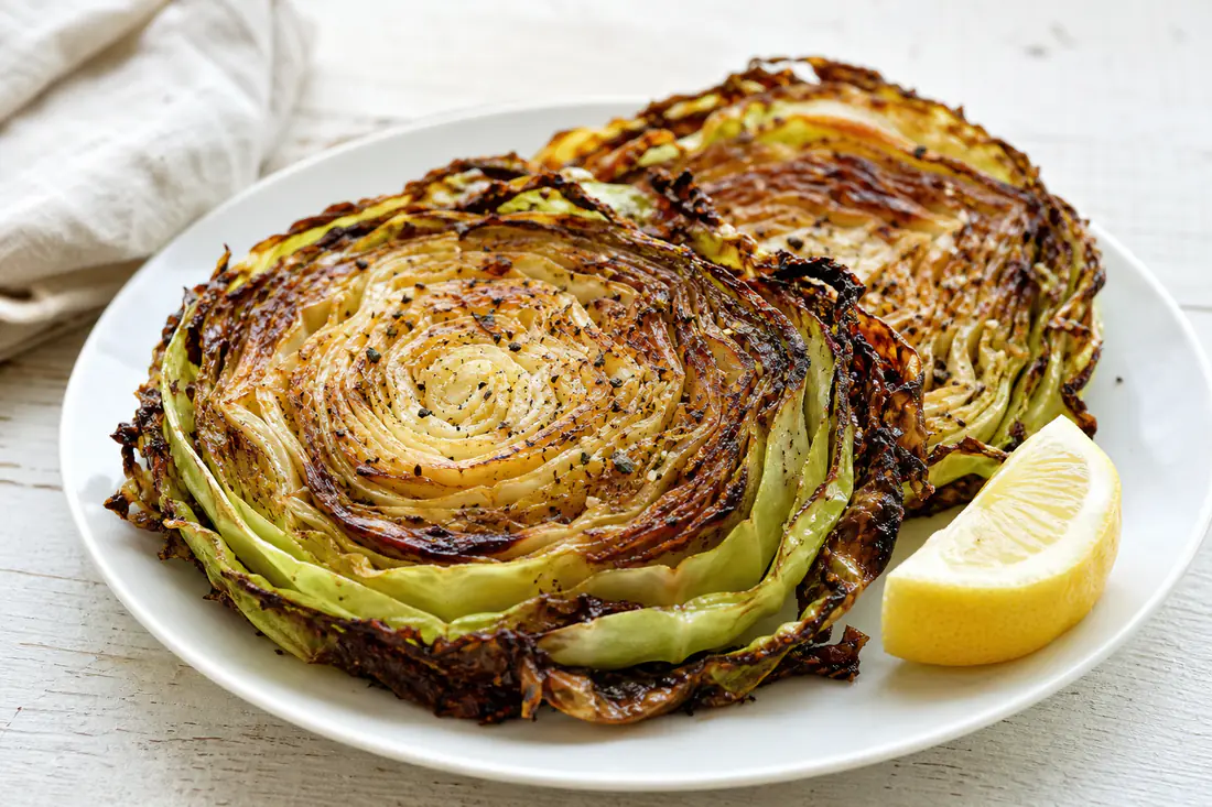 Thick roasted cabbage steaks with browned crispy edges and a lemon wedge on a white plate