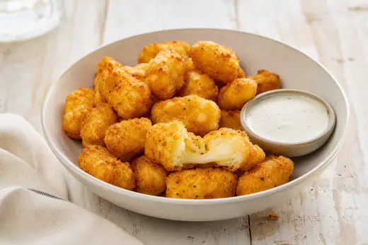 Golden breaded cheese curds in a bowl with a small dish of ranch dressing