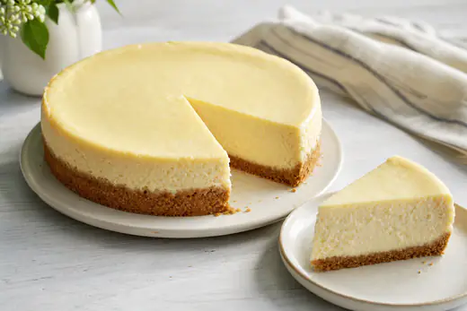 A small ROUND cheesecake with a graham cracker crust, with one creamy slice cut out on a plate