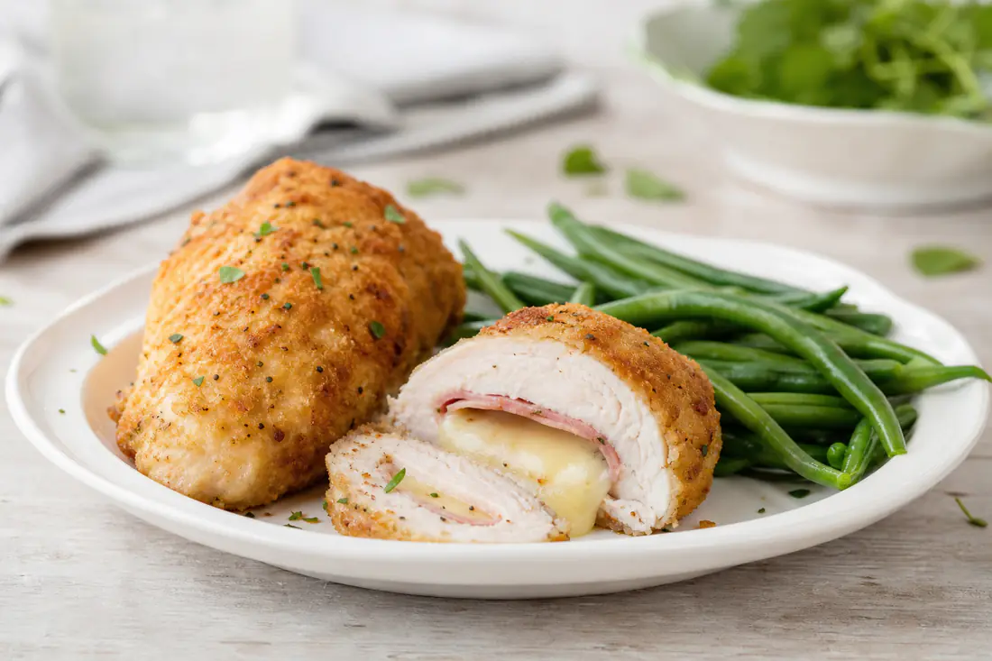 Sliced breaded chicken cordon bleu rolls showing melted Swiss cheese and ham, served with green beans