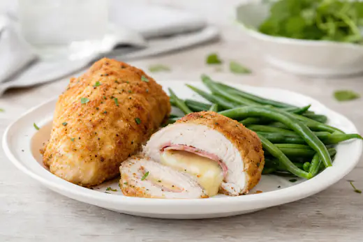 Sliced breaded chicken cordon bleu rolls showing melted Swiss cheese and ham, served with green beans
