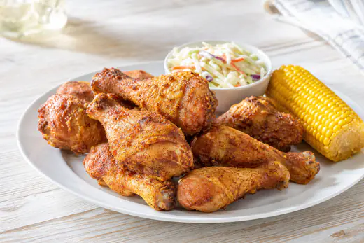 Crispy golden chicken drumsticks piled on a white plate with a side of coleslaw