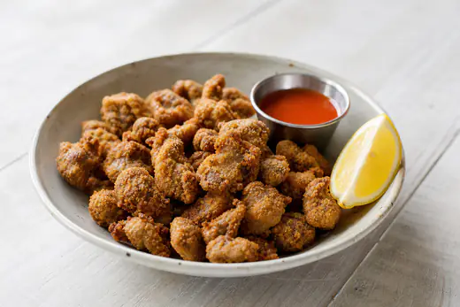 Golden crispy breaded chicken gizzards in a small bowl with hot sauce and a lemon wedge