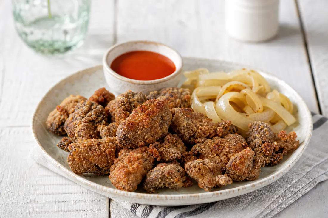 Crispy breaded chicken livers on a plate with sliced onions and hot sauce