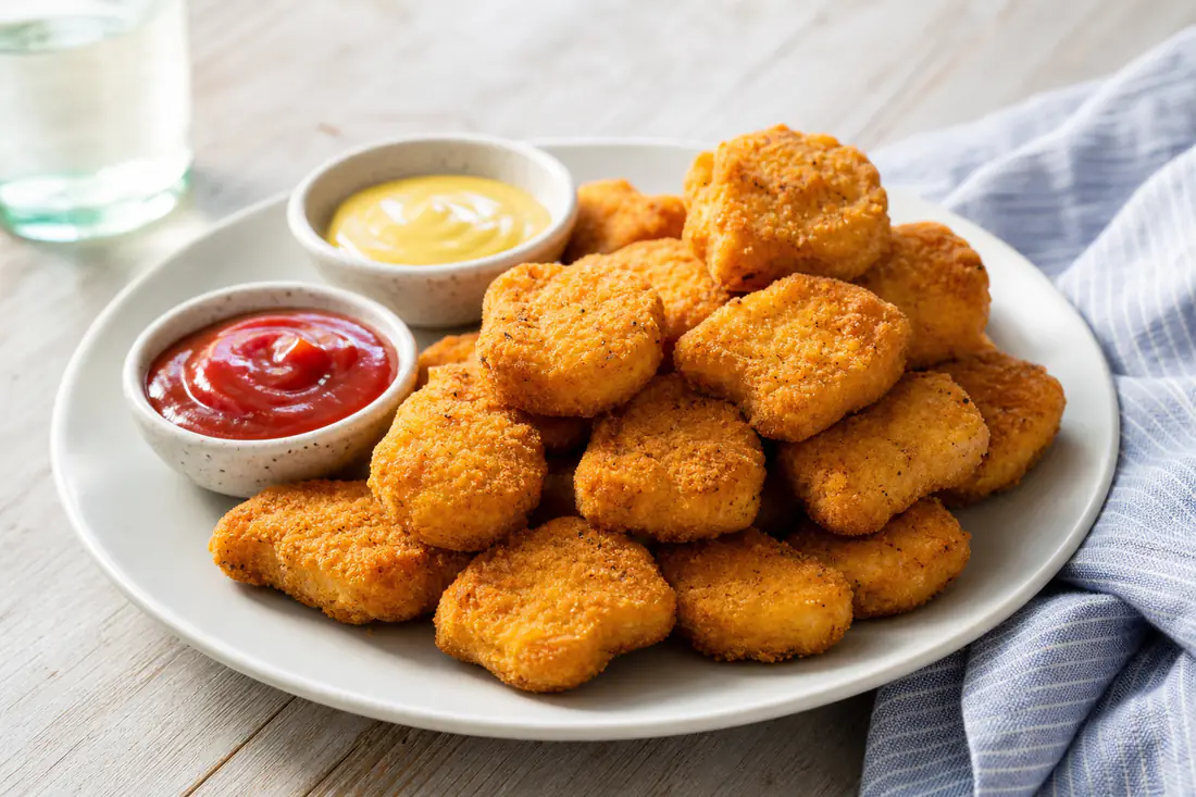 Golden homemade chicken nuggets stacked on a plate with ketchup and honey mustard