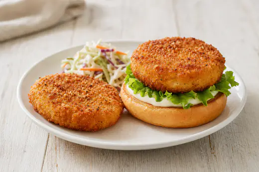 Two golden breaded chicken patties on a white plate with coleslaw and a bun