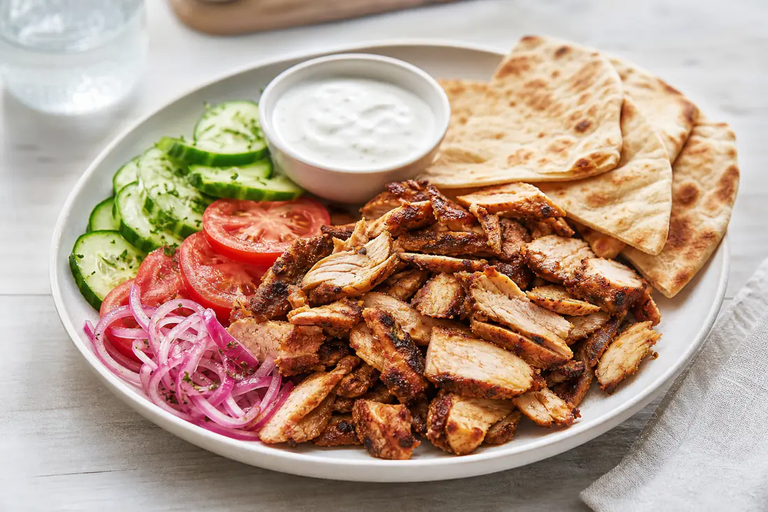 Sliced spiced chicken shawarma with pita, cucumber, tomato and garlic sauce