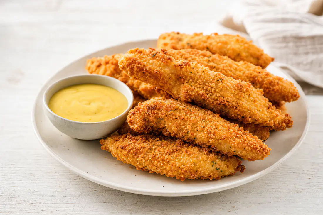 Golden panko-breaded chicken tenders on a plate with honey mustard dipping sauce