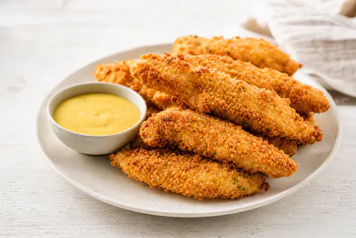Golden panko-breaded chicken tenders on a plate with honey mustard dipping sauce
