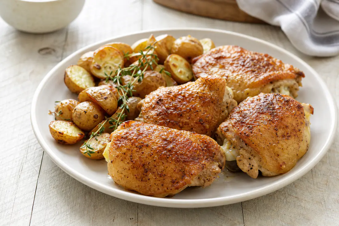 Crispy golden bone-in skin-on chicken thighs on a plate with roasted potatoes