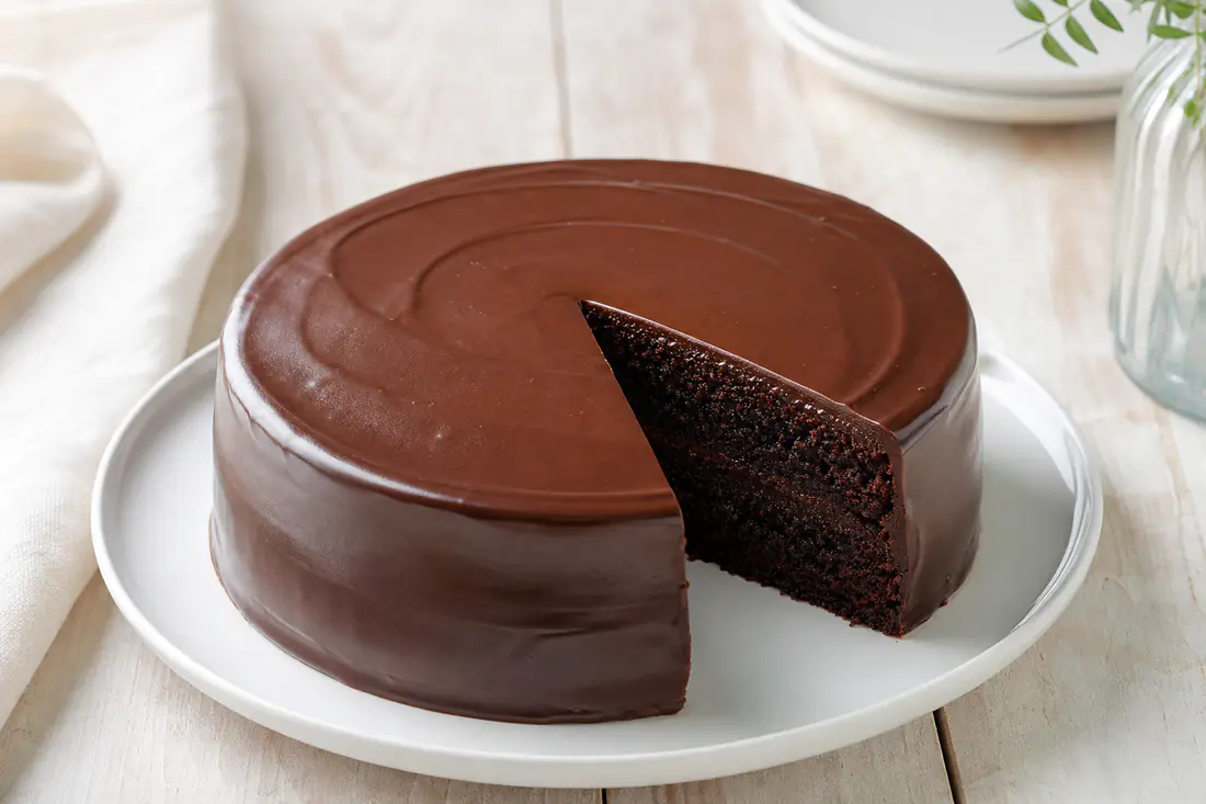 A small ROUND chocolate cake covered in glossy chocolate ganache, with one slice cut to show the moist crumb