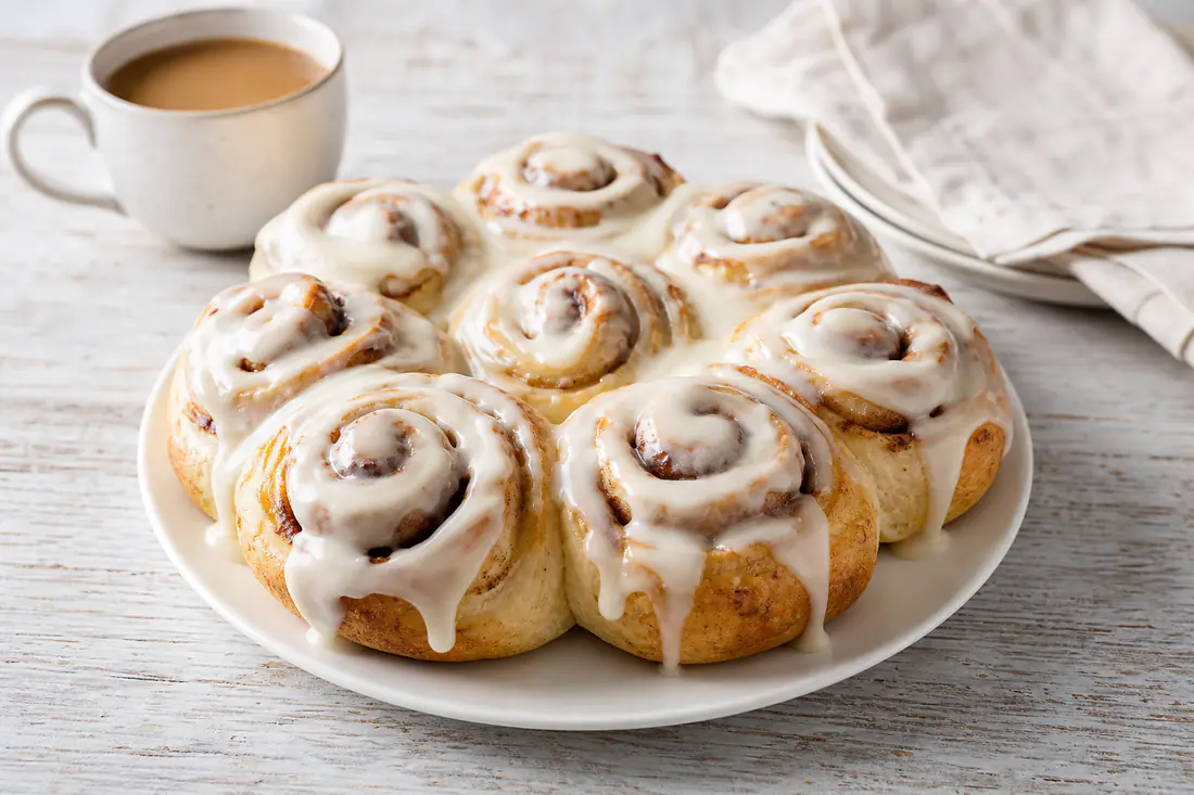 Soft golden cinnamon rolls topped with white cream cheese icing on a plate