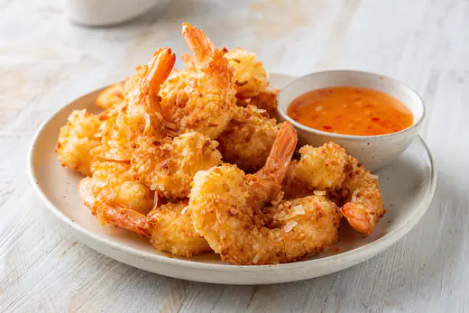 Golden coconut shrimp on a plate with a small bowl of sweet chili dipping sauce