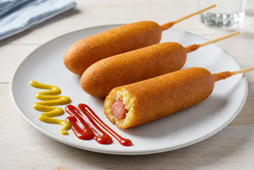 Golden corn dogs on sticks with yellow mustard and ketchup on a plate