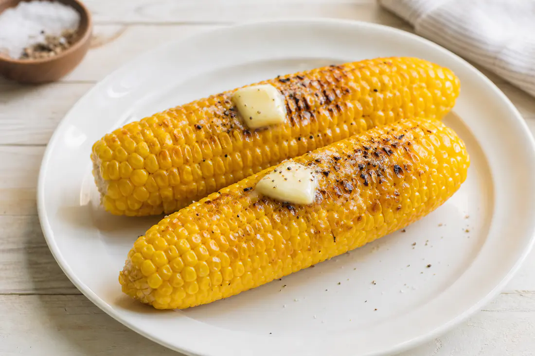 Golden corn on the cob with melted butter and light char marks on a white plate