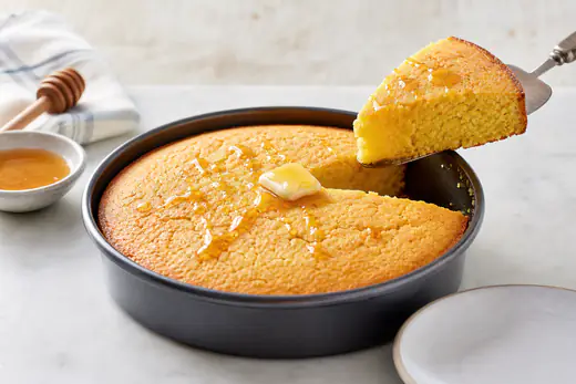 Golden round cornbread cut into wedges with a pat of butter