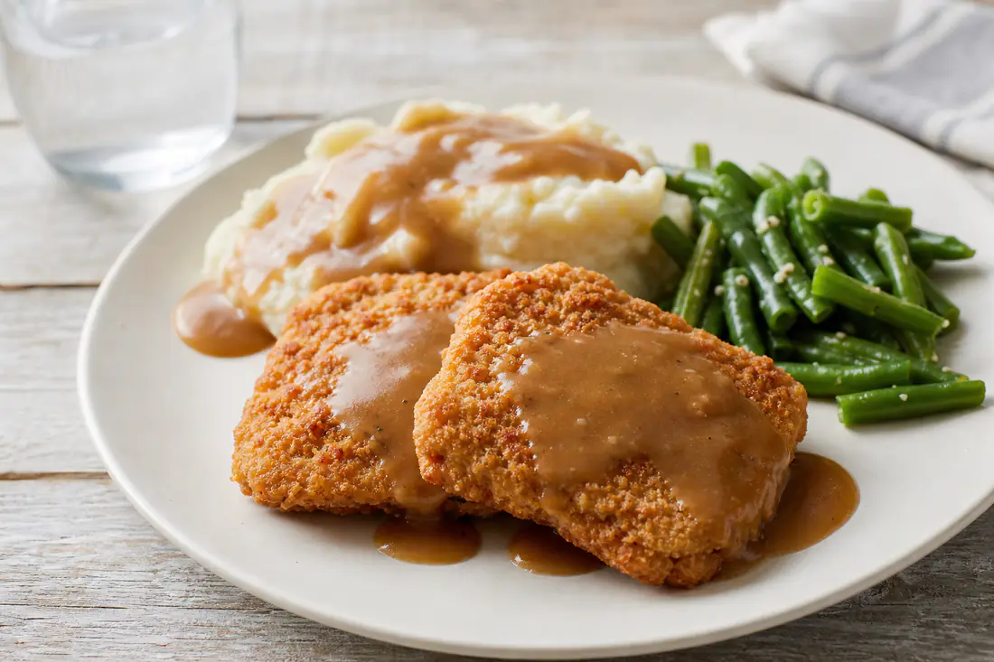 Golden breaded cube steaks on a plate with mashed potatoes and gravy