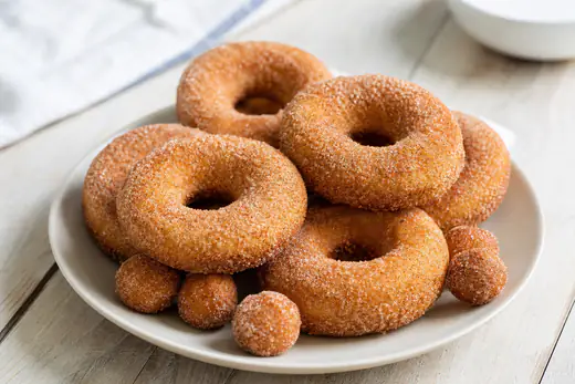 Golden ring donuts coated in cinnamon sugar on a plate, with a few donut holes beside them