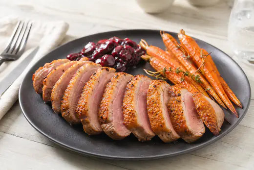 Sliced duck breast with crispy golden skin and a pink center on a dark plate