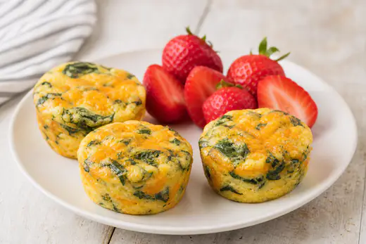Round fluffy egg bites with spinach and cheddar in silicone cups on a white plate