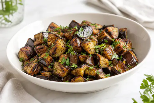 Roasted eggplant cubes with browned edges and chopped parsley in a white bowl