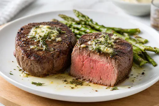 Two sliced filet mignon steaks with garlic butter and thyme on a white plate