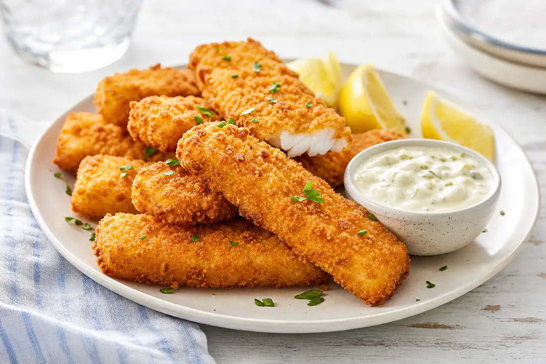 Golden crispy fish sticks with tartar sauce and lemon wedges