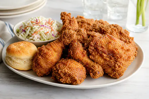 Crunchy golden fried chicken thighs and drumsticks with a craggy crust on a platter with coleslaw