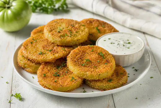 Golden cornmeal-breaded fried green tomato slices on a plate with a small bowl of ranch dip
